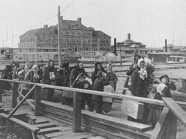 Photo: immigrants coming up the board-walk from the barge, which has taken them off the steamship company's docks, and transported them to Ellis Island, 1902. Credit: Library of Congress, Prints and Photographs Division.