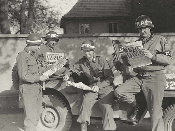 Photo: four MPs take a break along a German road to read in the "Stars and Stripes" newspaper about the Nazi surrender during WWII, May 1945. Credit: U.S. Army; Wikimedia Commons.