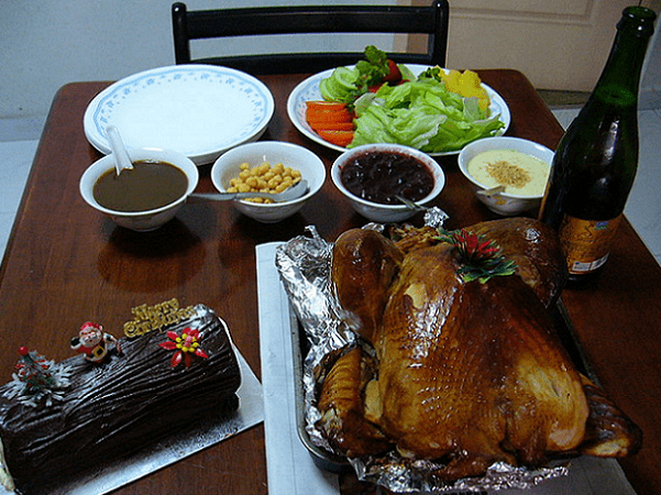 Photo: a roast turkey surrounded by Christmas log cake, gravy, sparkling juice, and vegetables. Credit: Chensiyuan; Wikimedia Commons.