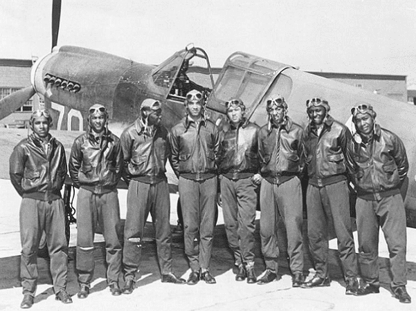Photo: Tuskegee Airmen in front of a P-40 fighter aircraft, c. May 1942 to Aug 1943. Location unknown, likely Southern Italy or North Africa. Credit: U.S. Air Force; Wikimedia Commons.
