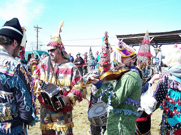 Photo: Wilson Savoy of the Pine Leaf Boys (Cajun accordion player in sunglasses and patchwork costume) playing with other Cajun musicians at the 2010 Faquetigue Courir de Mardi Gras in Savoy, Louisiana. Credit: Herb Roe; Wikimedia Commons.