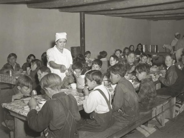 Photo: schoolchildren eating hot school lunches made up primarily of food from the surplus commodities program. Taken at a school in Penasco, New Mexico, December 1941. Credit: United States Department of Agriculture; Wikimedia Commons.