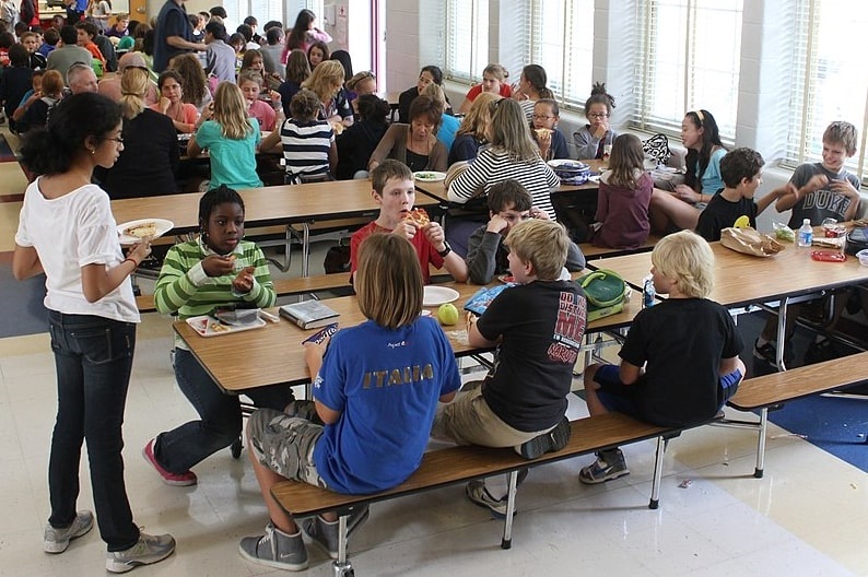 Photo: a group of middle schoolers eat lunch in their school lunchroom. Credit: woodleywonderworks; Wikimedia Commons.