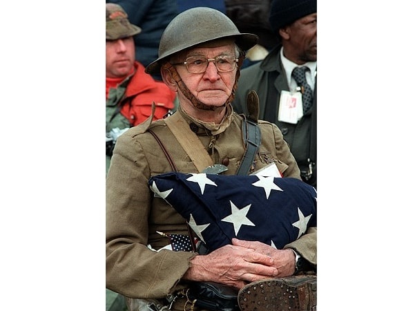 Photo: U.S. World War I veteran Joseph Ambrose (1896–1988) attends the dedication parade for the Vietnam Veterans Memorial in 1982, wearing his original Brodie helmet and doughboy uniform and holding the flag that covered the casket of his son, Clement, who was killed in the Korean War. Credit: National Archives and Records Administration; Wikimedia Commons.