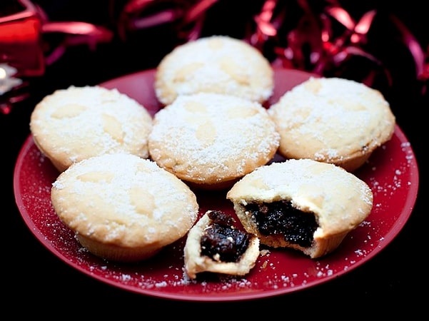 Photo: plate of mince pies with decorated crusts and spicy fruit filling served sprinkled with sugar, one broken open to reveal the filling. Credit: christmasstockimages.com; Wikimedia Commons.
