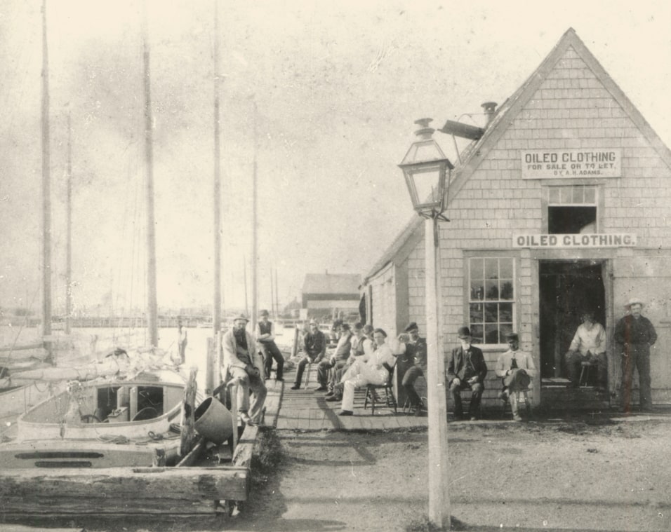 Photo: Adams Boat House at Adams Slip on Steamboat Wharf, Nantucket, where oiled clothing was available for sale or rent. Alden H. Adams is sitting in the doorway surrounded by old sea mariners. Courtesy of the Nantucket Historical Association.
