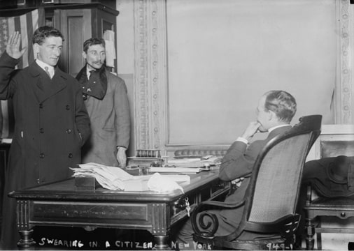 Photo: a man taking the required citizenship oath of allegiance in front of a U.S. government official in New York City, 8 February 1910. Credit: Library of Congress, Prints and Photographs Division.