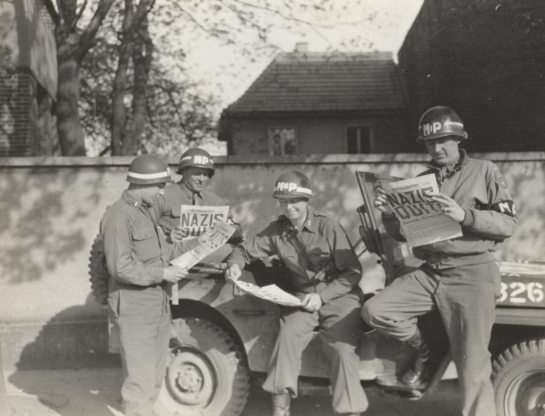 Photo: four MPs take a break along a German road to read in the “Stars and Stripes” newspaper about the Nazi surrender, May 1945. Credit: U.S. Army; Wikimedia Commons.