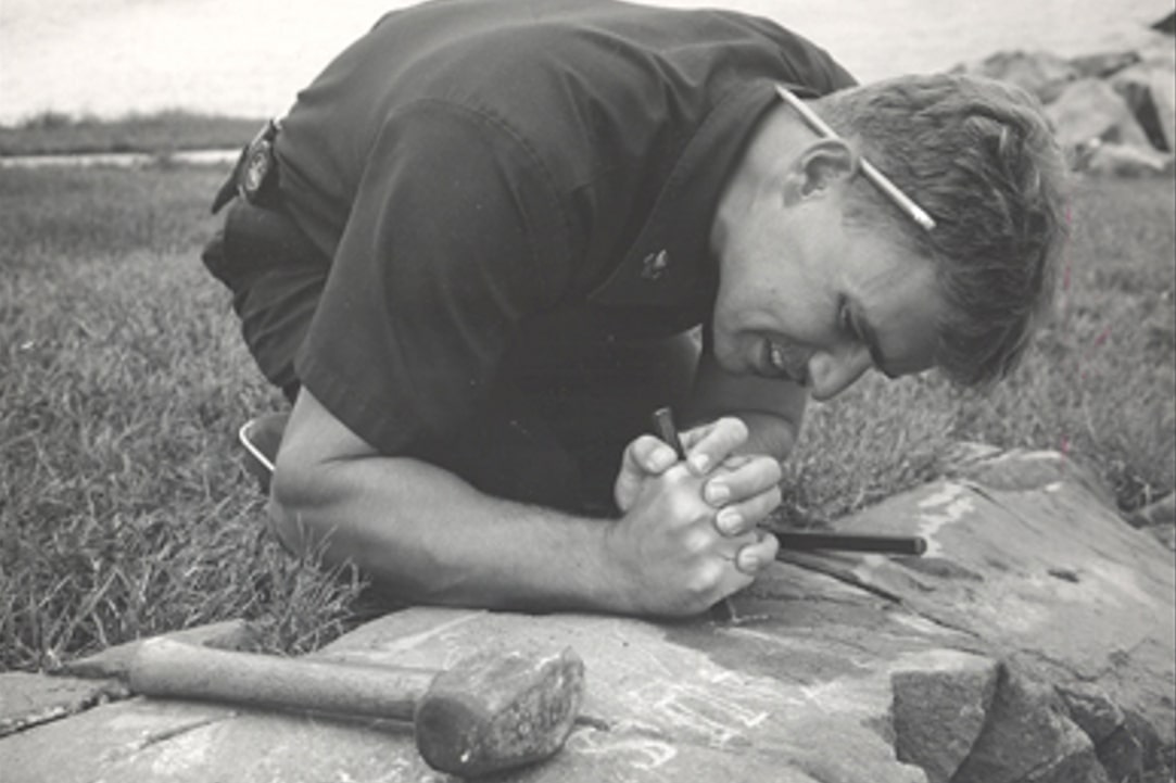 Photo: Dennis Dever carving his name and the date 1989 into a rock at Boston Light, carrying on a long tradition of keepers who left their mark – the oldest being Robert Ball in 1768. Credit: Jeremy D’Entremont; United State Lighthouse Society Collection.